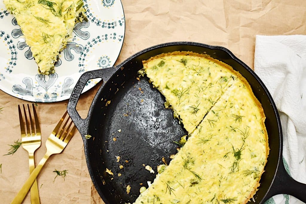 asparagus and spring onion frittata in black pan with slice taken out on plate