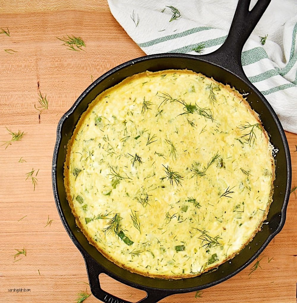 spring onion frittata in black cast iron pan on wood background.