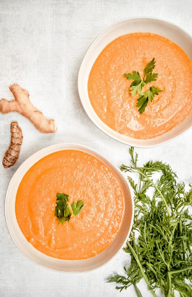 overhead shot of carrot ginger soup with piece of giner, turmeric, and carrot leaeves