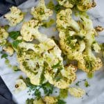 roasted cauliflower on marble background with green herb dressing drizzled on top