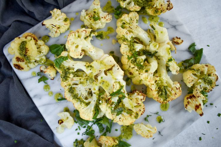 roasted cauliflower on marble background with green herb dressing drizzled on top