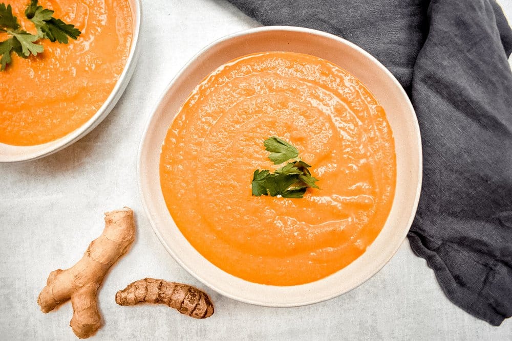 carrot ginger soup on grey background with grey linen and piece of ginger