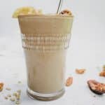 glass filled with banana bread chickpea smoothie on white background with stainless steel straw.