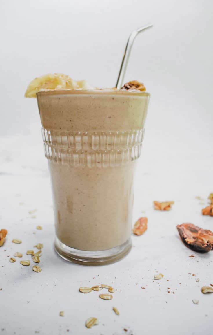 glass filled with banana bread chickpea smoothie on white background with stainless steel straw.