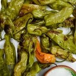 closeup of grilled shishito peppers with bowl of salt