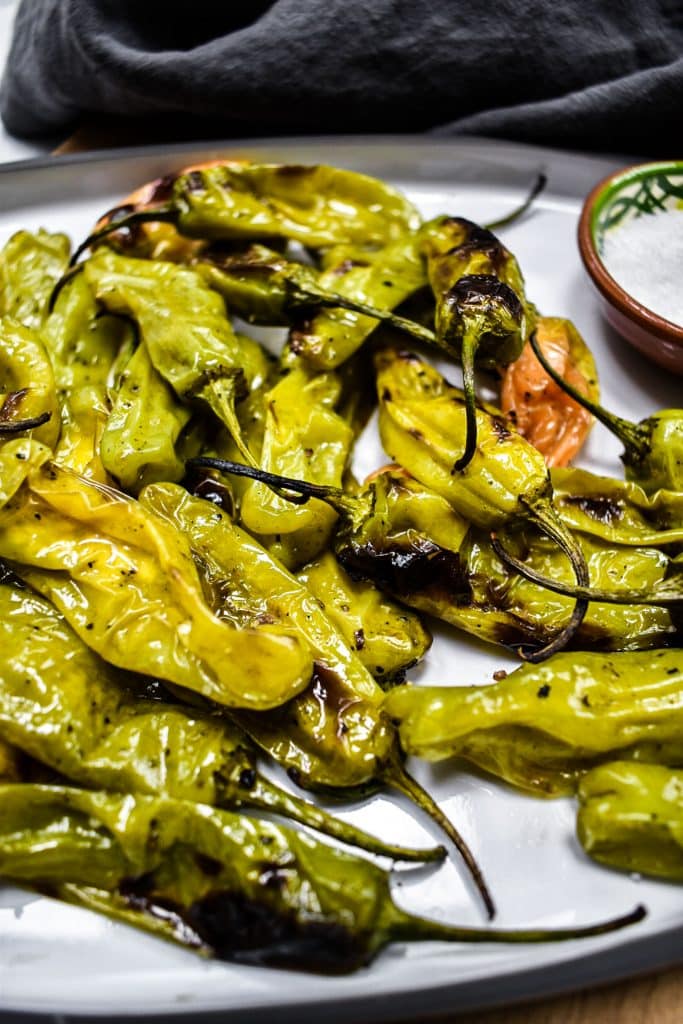 white serving dish with grilled shishito peppers and bowl of salt with grey napkin