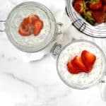 overhead shot of 2 jars of strawberry cheesecake overnight oats on marble background with basket of strawberries