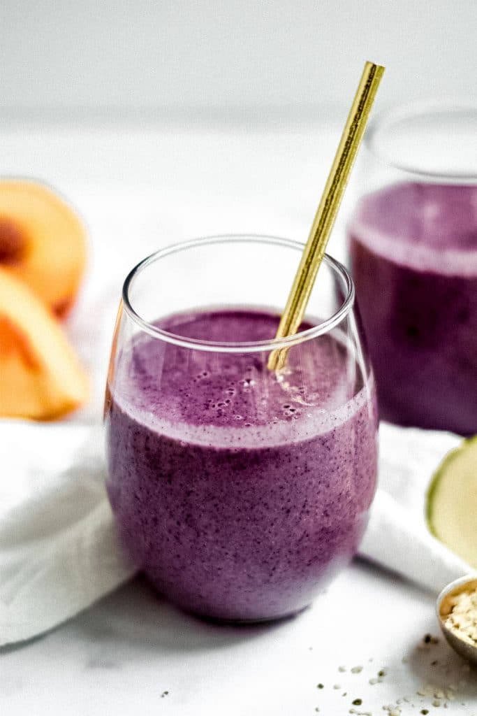 two smoothies in stemless wine glass with gold straws and slices of peach and zucchini