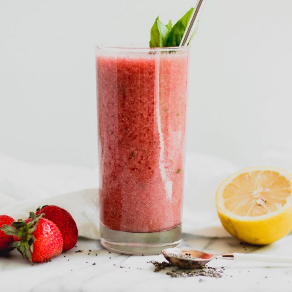 lemonade smoothie in a glass with strawberries, basil, and lemon on a marble slab