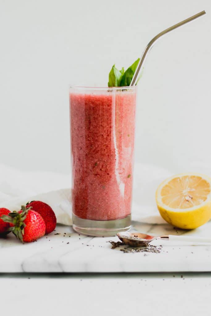lemonade smoothie in a glass with strawberries, basil, and lemon on a marble slab