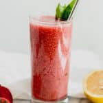 smoothie in tall glass with basil leaf and straw on marble background