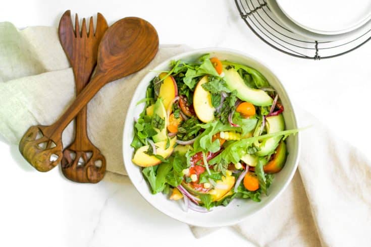 overhead shot of grilled peach salad with wooden spoons on marble background