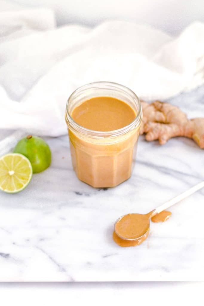 peanut ginger sauce in jar with spoon covered in sauce next to jar and lime and ginger. 