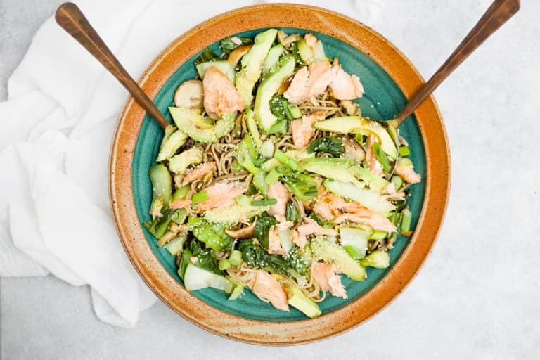 soba noodle salad in a bowl on gray background with serving spoons in bowl